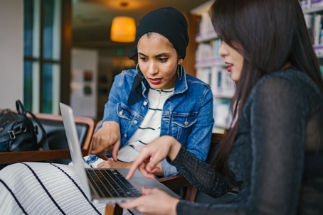 two women working at laptop pointing at screen